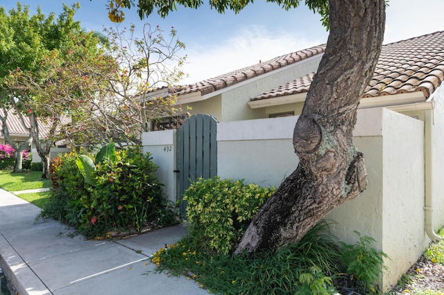 view of home's exterior featuring a tile roof, a gate, fence, and stucco siding