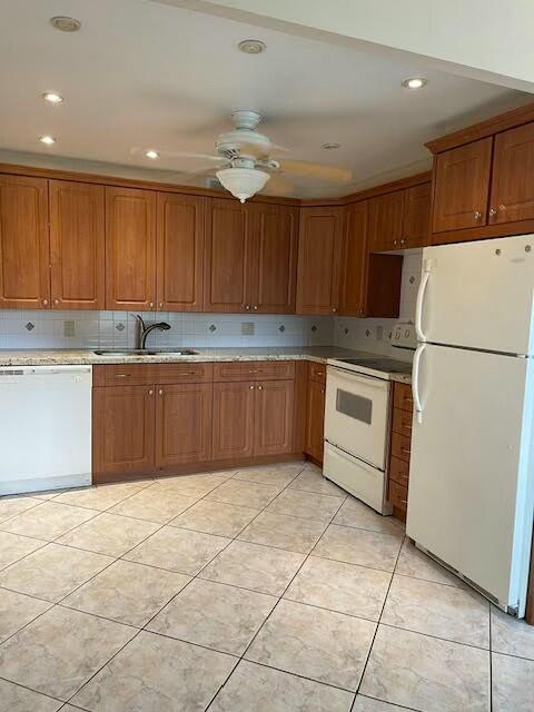 kitchen with brown cabinetry, white appliances, and a sink