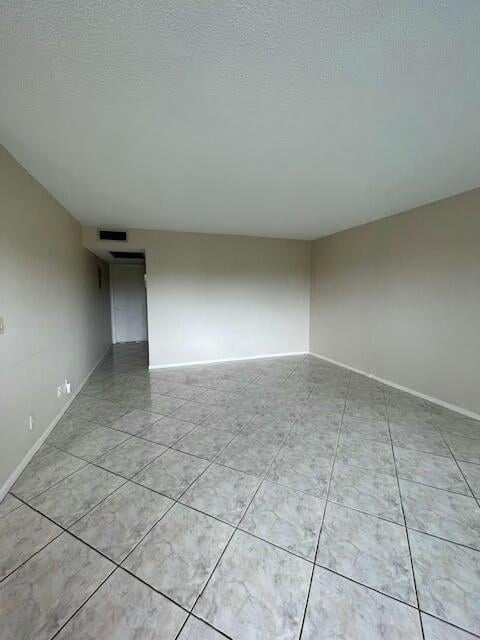 empty room with visible vents, light tile patterned flooring, a textured ceiling, and baseboards