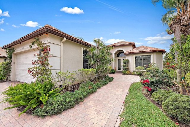 mediterranean / spanish-style house featuring a garage, a tiled roof, french doors, decorative driveway, and stucco siding