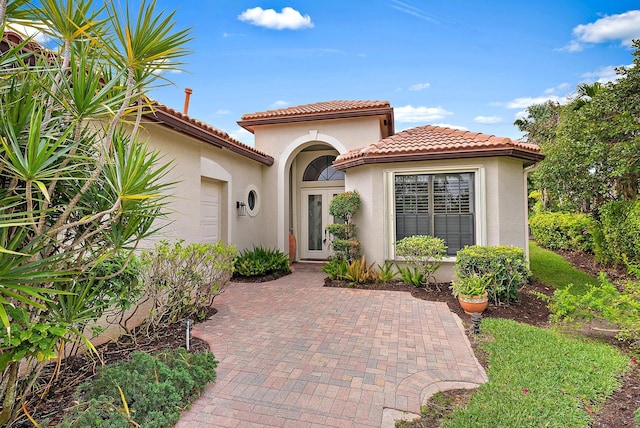 property entrance with an attached garage, a tile roof, and stucco siding