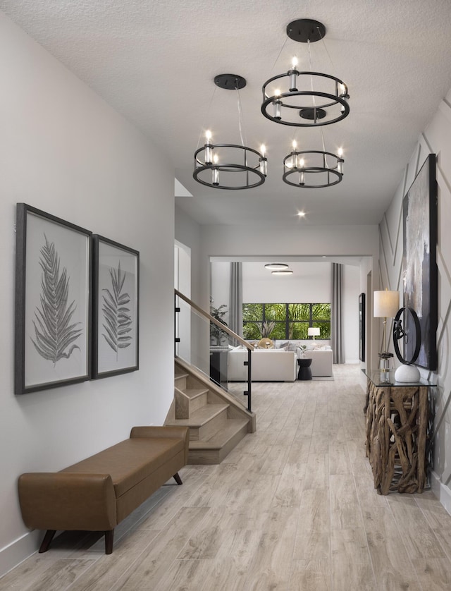 hall featuring an inviting chandelier, a textured ceiling, stairway, and wood finished floors