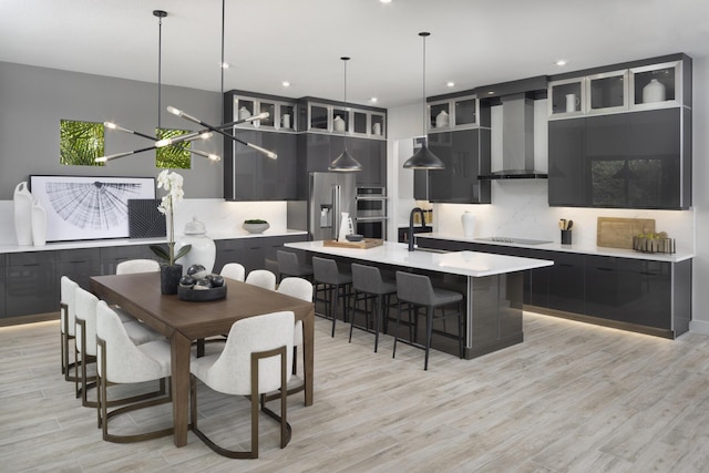 kitchen with stainless steel appliances, a sink, dark cabinetry, wall chimney exhaust hood, and modern cabinets