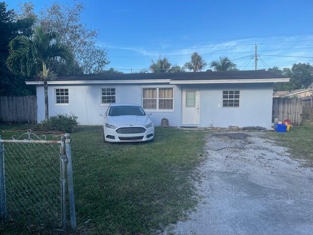 ranch-style home with driveway, a front lawn, fence, and stucco siding