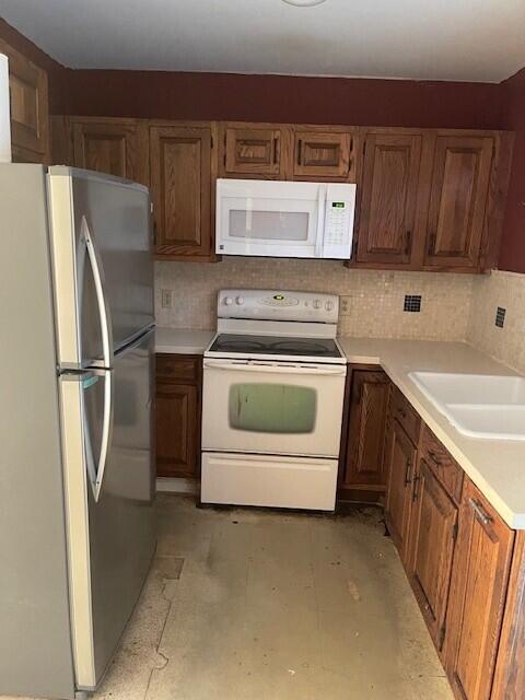 kitchen featuring white appliances, decorative backsplash, brown cabinetry, light countertops, and a sink