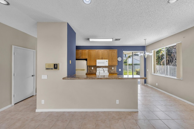 kitchen with a peninsula, white appliances, a sink, decorative backsplash, and brown cabinetry