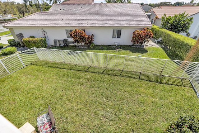 rear view of property featuring a fenced backyard, a lawn, a tiled roof, and stucco siding