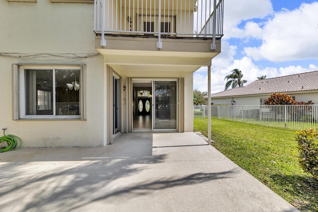 entrance to property featuring a patio, fence, a lawn, and stucco siding