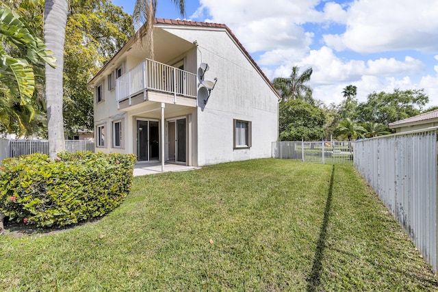 back of house with a yard, a fenced backyard, a balcony, and stucco siding