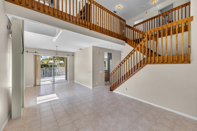 unfurnished living room featuring stairway, tile patterned flooring, a high ceiling, and baseboards