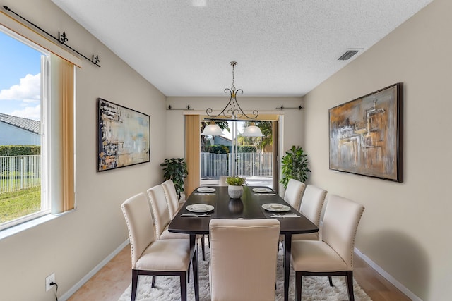 tiled dining area featuring a wealth of natural light, visible vents, a textured ceiling, and baseboards