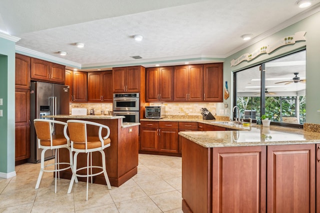 kitchen featuring a breakfast bar area, appliances with stainless steel finishes, a sink, light stone countertops, and a peninsula