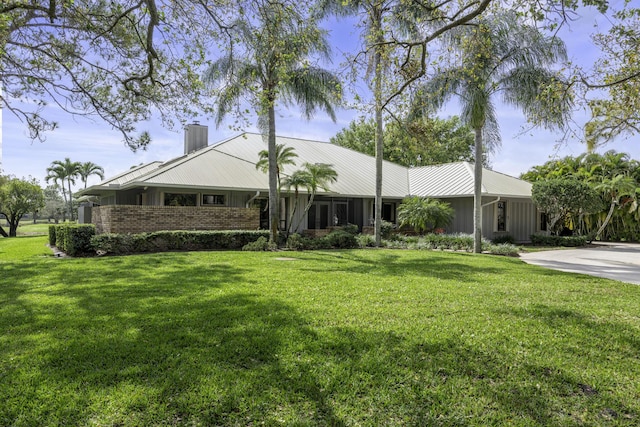 ranch-style home featuring brick siding, metal roof, a chimney, and a front lawn