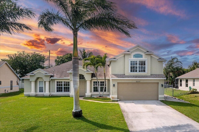 traditional-style home with stucco siding, a shingled roof, concrete driveway, an attached garage, and a front yard