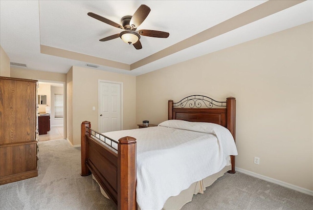 bedroom featuring light carpet, visible vents, a tray ceiling, and baseboards