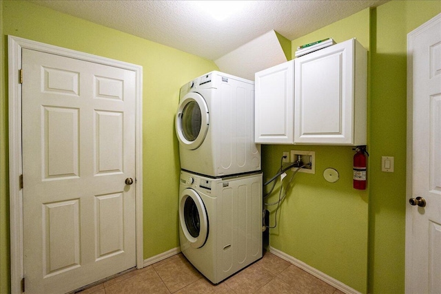 laundry area featuring cabinet space, a textured ceiling, baseboards, and stacked washer / dryer