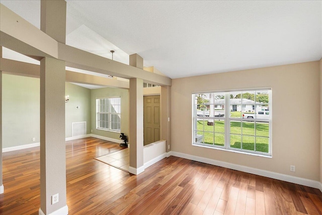 empty room featuring lofted ceiling, wood finished floors, visible vents, and baseboards