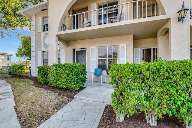 entrance to property with a balcony, central AC, and stucco siding