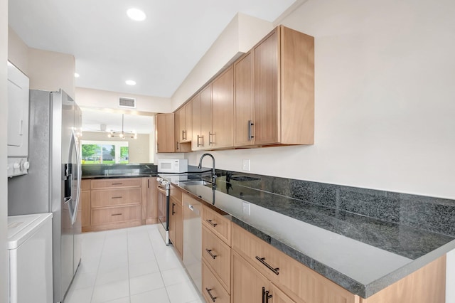 kitchen featuring light brown cabinets, visible vents, a sink, stacked washer and dryer, and appliances with stainless steel finishes