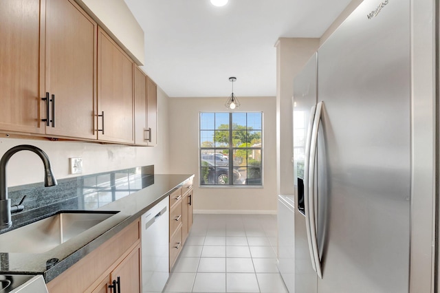 kitchen with dishwashing machine, dark stone countertops, light tile patterned floors, a sink, and stainless steel fridge