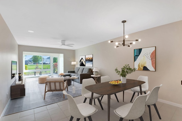 dining space featuring light tile patterned flooring, ceiling fan with notable chandelier, and baseboards