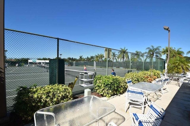 view of patio / terrace with a tennis court, outdoor dining space, and fence