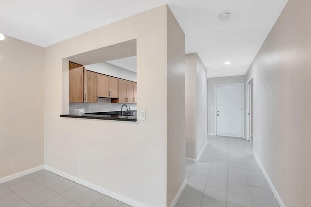 hallway featuring light tile patterned flooring, baseboards, and a sink