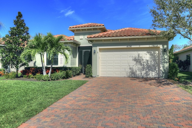 mediterranean / spanish-style house featuring a tiled roof, an attached garage, decorative driveway, a front yard, and stucco siding