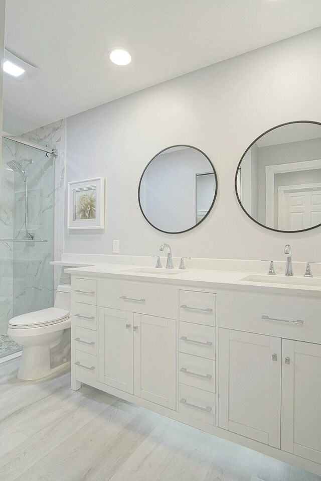 bathroom featuring a marble finish shower, double vanity, a sink, and toilet