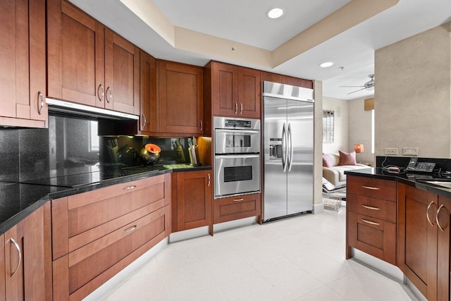 kitchen featuring ceiling fan, under cabinet range hood, appliances with stainless steel finishes, brown cabinetry, and dark countertops