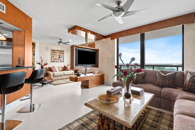 living room with a textured ceiling, tile patterned flooring, visible vents, and a ceiling fan