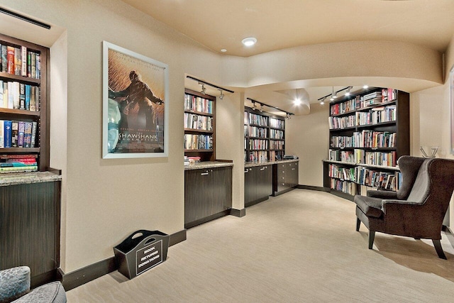 living area featuring baseboards, bookshelves, built in shelves, and light colored carpet