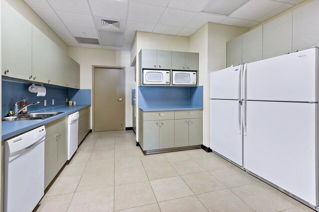 kitchen featuring white appliances, tasteful backsplash, visible vents, a paneled ceiling, and a sink