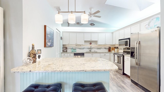 kitchen featuring white cabinets, a peninsula, a sink, stainless steel appliances, and backsplash