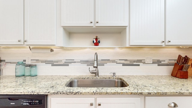 kitchen featuring black dishwasher, tasteful backsplash, white cabinets, a sink, and light stone countertops