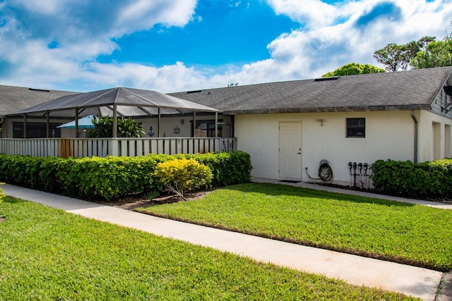 view of front of home featuring a shingled roof, glass enclosure, a front lawn, and stucco siding