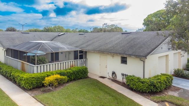 ranch-style home with glass enclosure, roof with shingles, a front lawn, and stucco siding