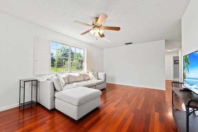 living room featuring a textured ceiling, ceiling fan, visible vents, baseboards, and dark wood finished floors