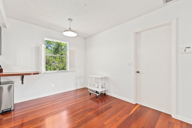 interior space with a textured ceiling, hardwood / wood-style floors, and baseboards