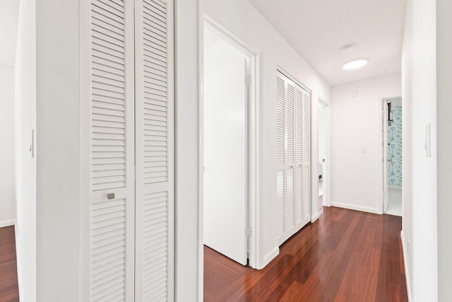 hallway featuring a textured ceiling, dark wood-style flooring, and baseboards