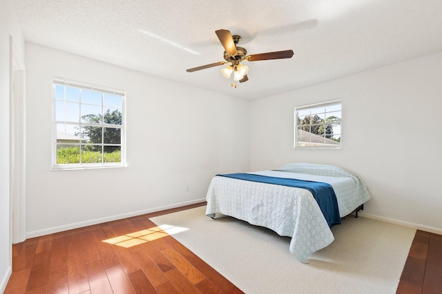 bedroom featuring ceiling fan, a textured ceiling, baseboards, and hardwood / wood-style floors