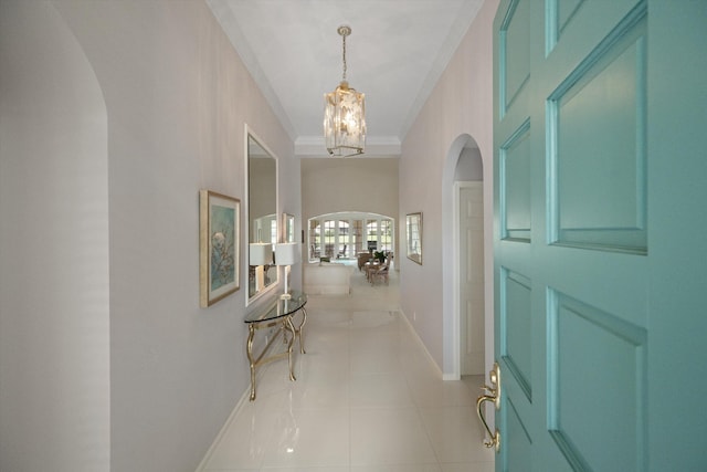 hall with arched walkways, a chandelier, light tile patterned flooring, baseboards, and ornamental molding