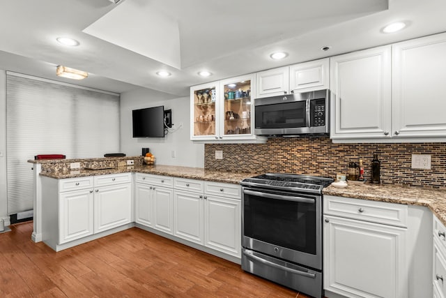 kitchen featuring stainless steel appliances, tasteful backsplash, light wood-type flooring, and a peninsula