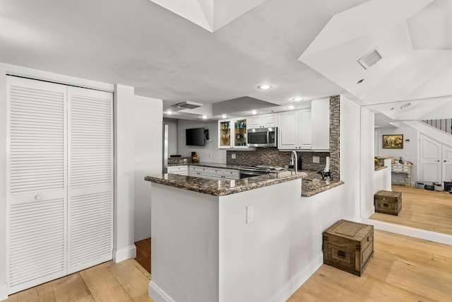 kitchen with stainless steel appliances, a peninsula, visible vents, light wood-type flooring, and dark stone countertops