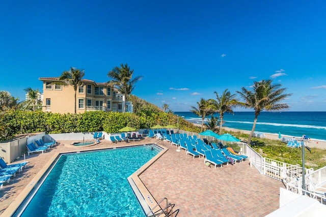 pool with a patio area, a community hot tub, a water view, and fence