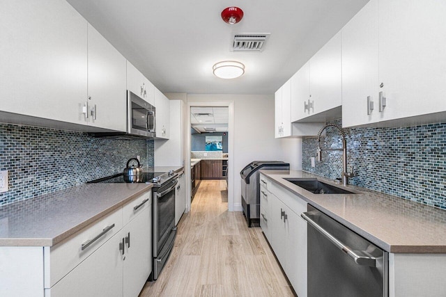 kitchen with light wood finished floors, visible vents, appliances with stainless steel finishes, a sink, and backsplash