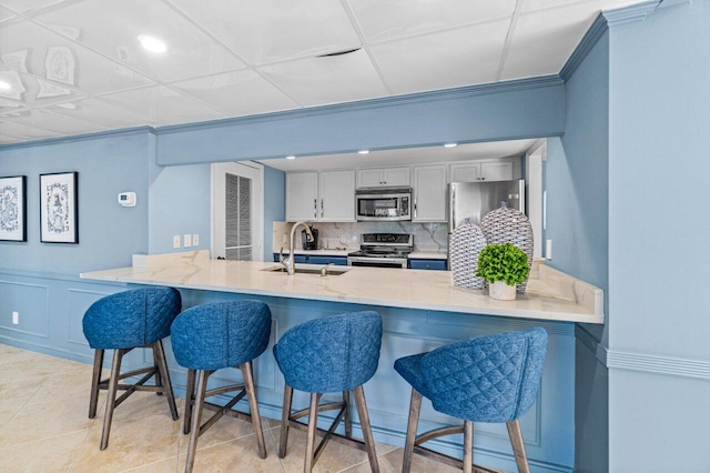 kitchen with a peninsula, a sink, a kitchen breakfast bar, appliances with stainless steel finishes, and decorative backsplash