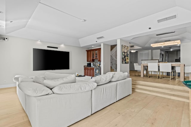 living area with light wood-style floors, a raised ceiling, visible vents, and stairway