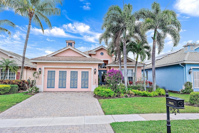 single story home with a tiled roof, an attached garage, decorative driveway, a front lawn, and stucco siding