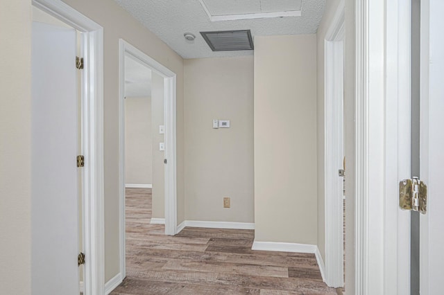 corridor featuring a textured ceiling, wood finished floors, visible vents, and baseboards